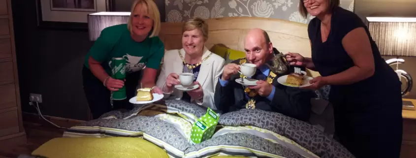A group of people standing on a bed with a cup of tea.