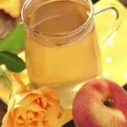 A cup of tea next to a peach and a rose.