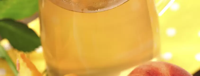 A cup of tea next to a peach and a rose.