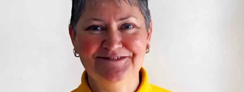 A woman in a yellow polo shirt smiling.
