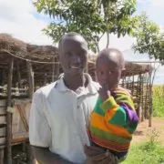 A man holding a child in front of a hut.