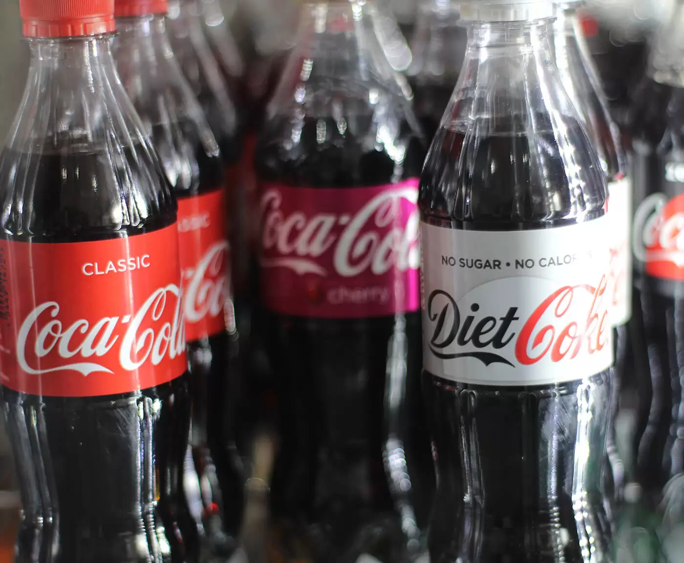 cold-drinks A row of coca cola bottles displayed in a vending machine.