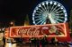 A Coca-Cola truck in front of a ferris wheel at Christmas.