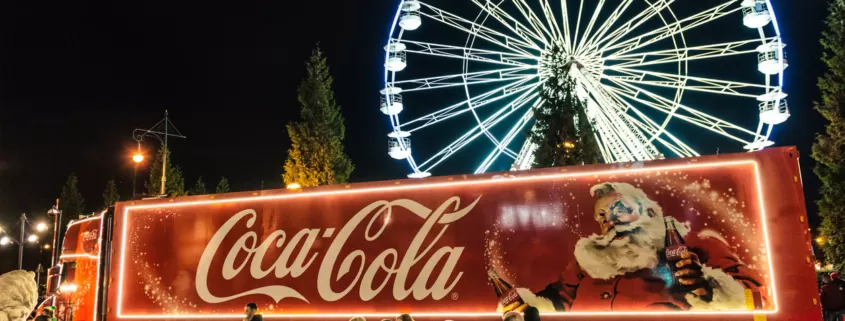A Coca-Cola truck in front of a ferris wheel at Christmas.