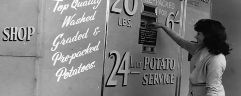 A woman checking out a potato vending machine from 1962.