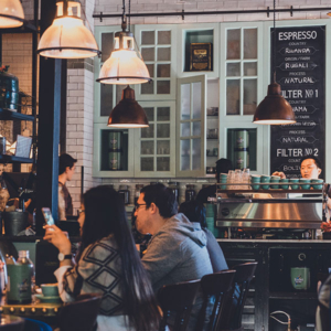 A group of people sipping coffee at a table in a restaurant with a Gaggia MD64 espresso machine nearby.