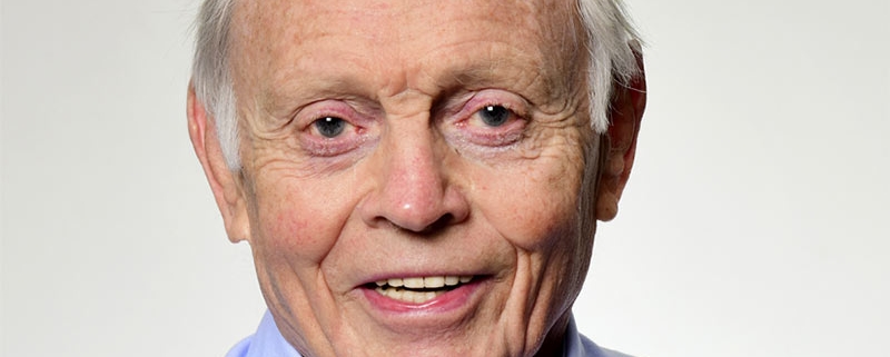 An older man in a blue shirt is smiling during the funeral.