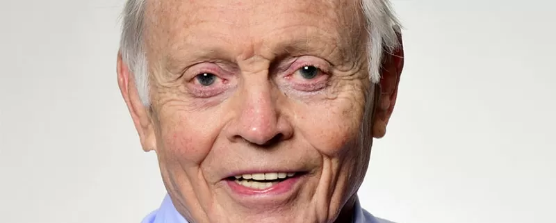 An older man in a blue shirt is smiling during the funeral.