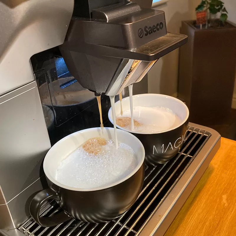 Two cups of coffee being poured from an espresso machine.