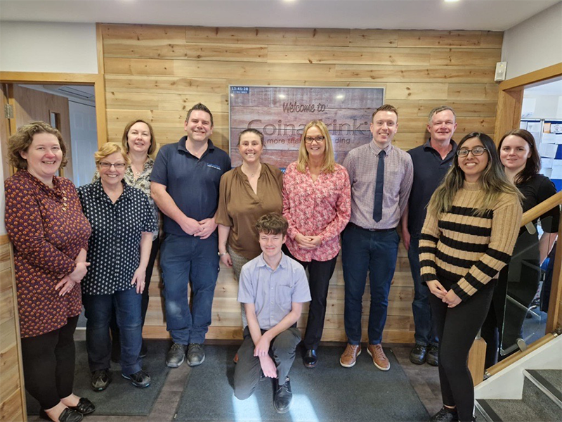 coinadrink-limited-real-living-wage-employer A group of people posing for a photo in an office, showcasing A Real Living Wage Employer.