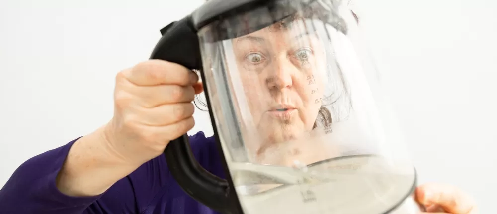 Woman looking through dirty kettle covered in limescale