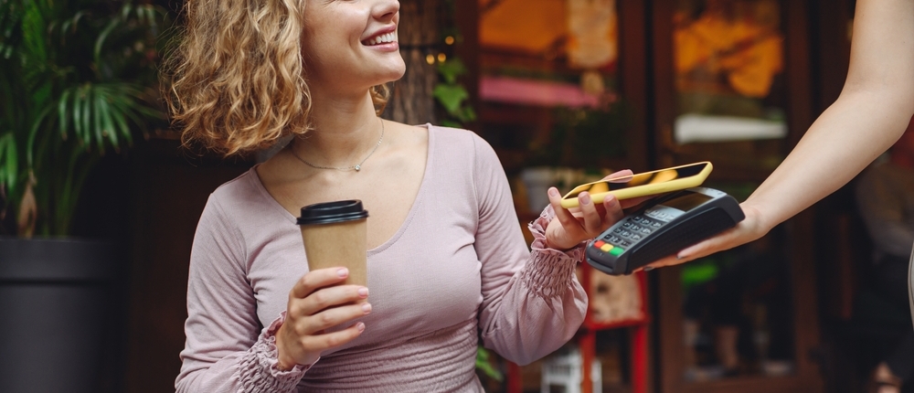 Young woman paying for takeaway coffee with contactless card